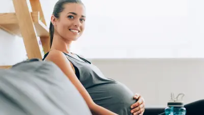 Side shot friendly smiling pregnant woman embracing her belly sitting on couch.