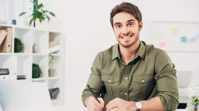 Friendly and helpful looking service employee in khaki colored shirt, sitting at desk.
